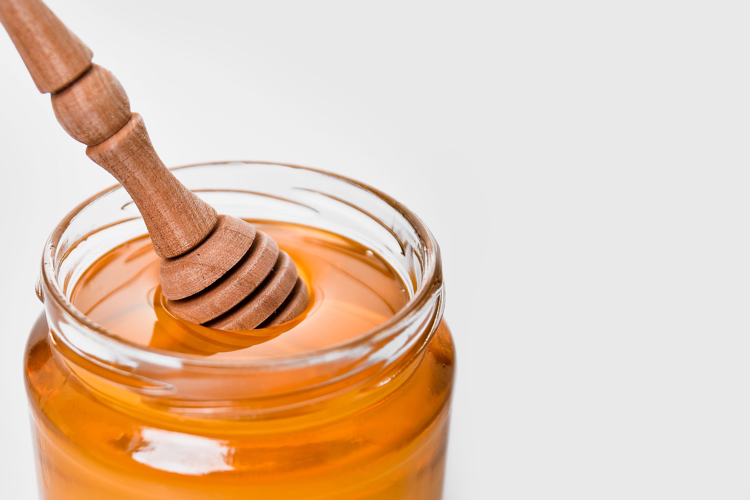 A glass jar of honey with a wooden dipper on a pale background